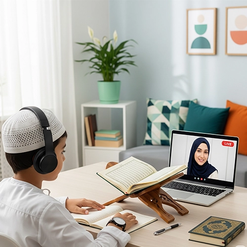 A young Muslim boy wearing a white topi and headphones, learning the Madni Qaida Course Online from a female teacher online, with a physical Madni Qaida open on a rehal in front of him.