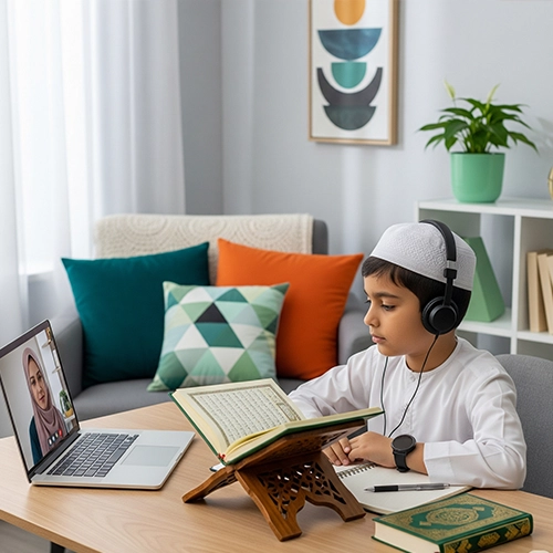A young Muslim boy wearing a white topi and headphones, studying Madni Qaida with a physical book and a notebook, while a female teacher is visible on a laptop screen.