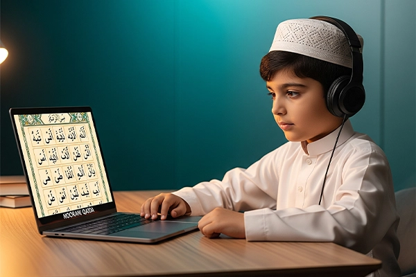 A young boy wearing a white topi and headphones, focused intently on an online Noorani Qaida lesson displayed on his laptop.